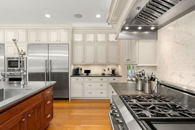 kitchen featuring tasteful backsplash, built in appliances, light wood-type flooring, custom range hood, and white cabinetry