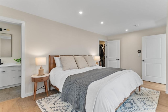 bedroom with light wood-style floors, recessed lighting, baseboards, and ensuite bath