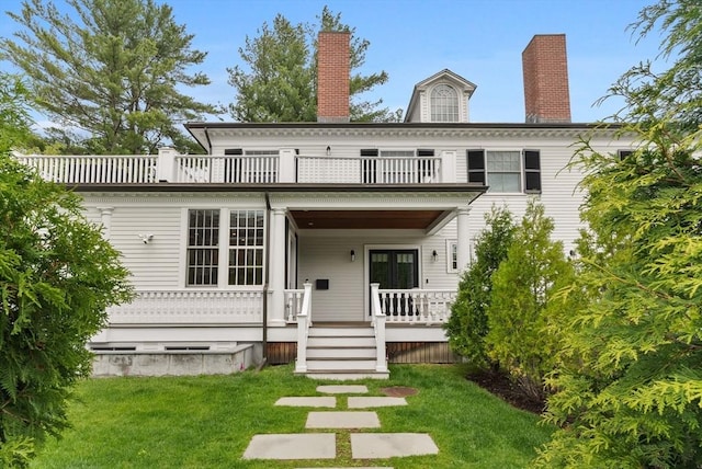 back of house featuring a balcony, a yard, a chimney, and a porch