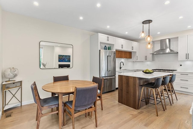 kitchen with wall chimney range hood, appliances with stainless steel finishes, a sink, a breakfast bar, and light wood-type flooring