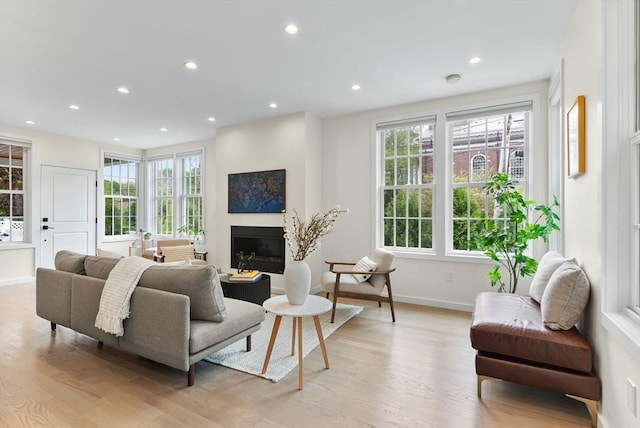 living area featuring light wood-style flooring, a glass covered fireplace, baseboards, and recessed lighting