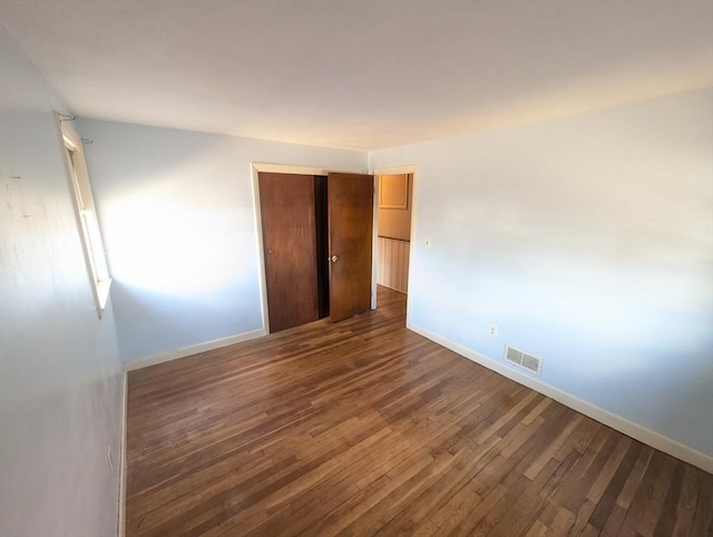 unfurnished bedroom featuring dark wood-style floors, visible vents, baseboards, and a closet