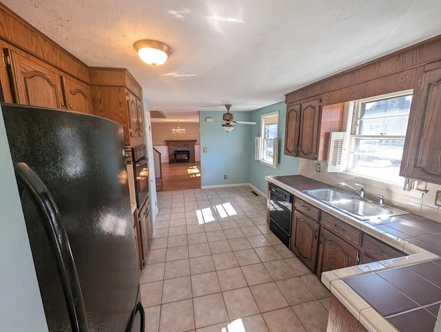 kitchen with light tile patterned floors, a fireplace, a sink, black appliances, and tile counters