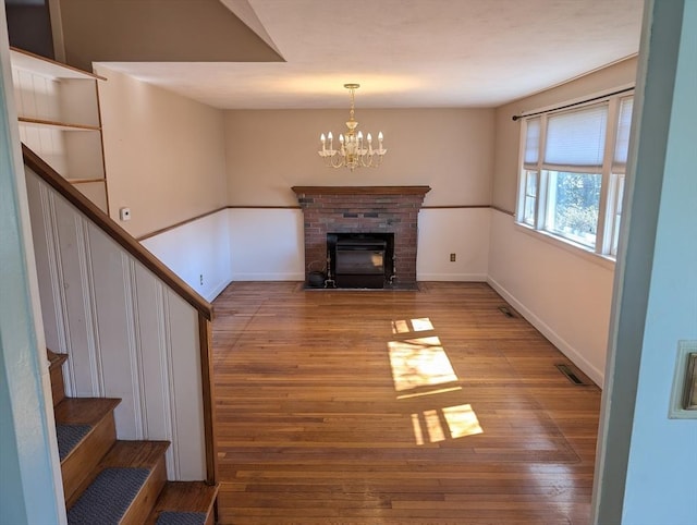 unfurnished living room with hardwood / wood-style flooring, an inviting chandelier, baseboards, a brick fireplace, and stairs