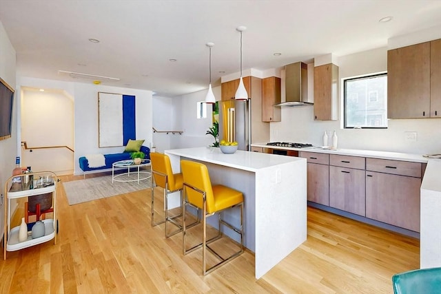 133 Charles St Unit 133, Cambridge, MA 02141 - kitchen featuring wall chimney range hood, light wood-type flooring, a kitchen bar, a kitchen island, and light countertops