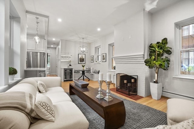 living room with a brick fireplace, a baseboard radiator, a chandelier, and light wood-type flooring