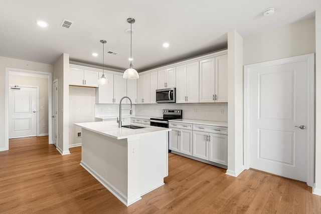 kitchen featuring white cabinets, a center island with sink, sink, light wood-type flooring, and appliances with stainless steel finishes