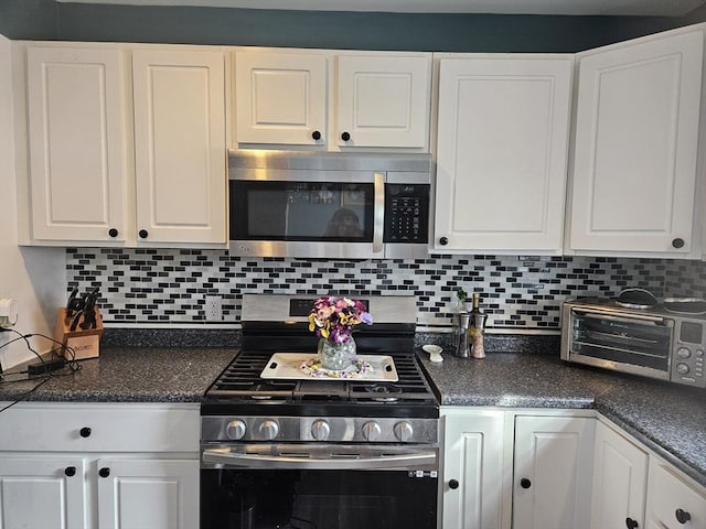 kitchen featuring dark countertops, a toaster, decorative backsplash, appliances with stainless steel finishes, and white cabinets