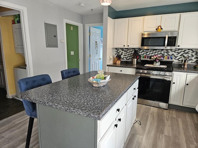 kitchen with stacked washer / dryer, a breakfast bar, electric panel, wood finished floors, and stainless steel appliances