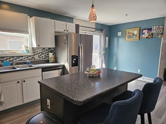 kitchen with a sink, a kitchen breakfast bar, dark countertops, backsplash, and stainless steel appliances