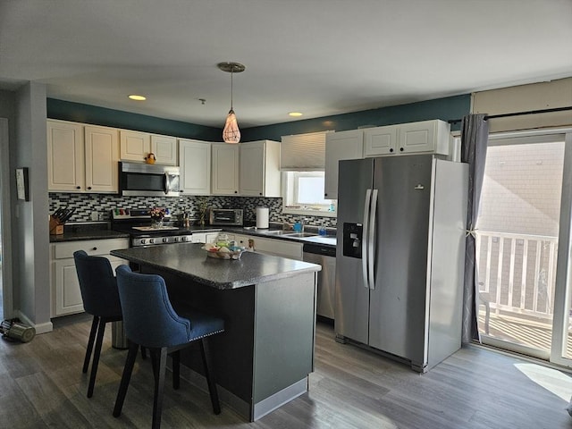 kitchen with tasteful backsplash, dark countertops, dark wood-style floors, a center island, and appliances with stainless steel finishes