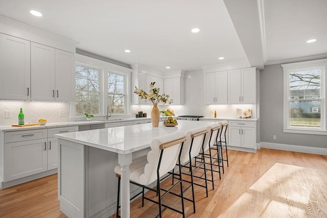 kitchen with decorative backsplash, light wood-type flooring, a breakfast bar, a center island, and white cabinetry