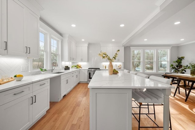 kitchen with light stone countertops, tasteful backsplash, white cabinetry, a kitchen island, and stainless steel range with gas stovetop