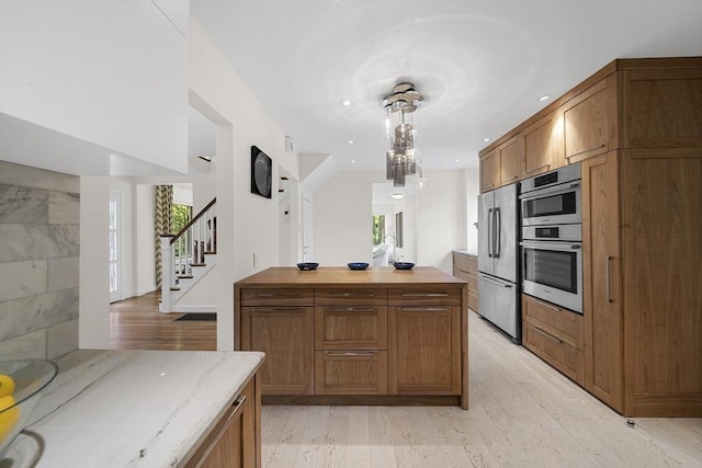 25 Day St, Newton, MA 02466 - kitchen with appliances with stainless steel finishes, brown cabinets, light stone counters, hanging light fixtures, and light wood-type flooring