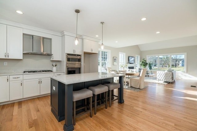 62 High St Lot 6, Stoneham, MA 02180 - kitchen with wall chimney exhaust hood, double oven, gas stovetop, light wood-style flooring, and white cabinets
