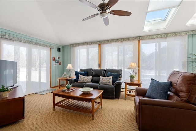 carpeted living room with ceiling fan, plenty of natural light, and vaulted ceiling with skylight