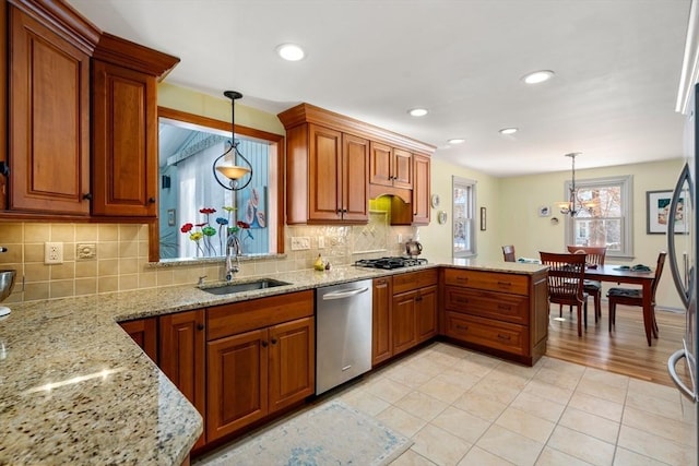 kitchen with light stone counters, sink, hanging light fixtures, and appliances with stainless steel finishes