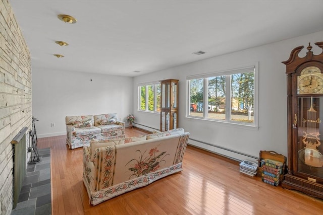 bedroom with a brick fireplace, light wood-type flooring, and baseboard heating