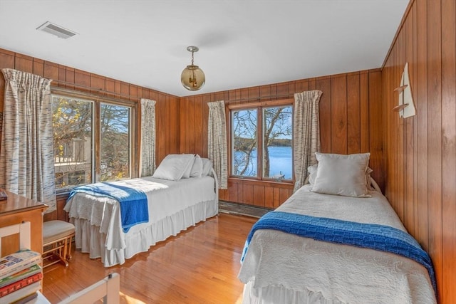 bedroom featuring a baseboard radiator, wooden walls, and light hardwood / wood-style floors