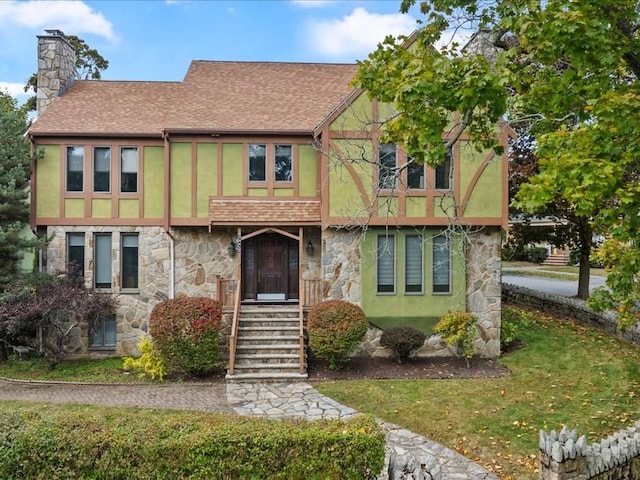 tudor-style house with a shingled roof, stone siding, a chimney, and stucco siding