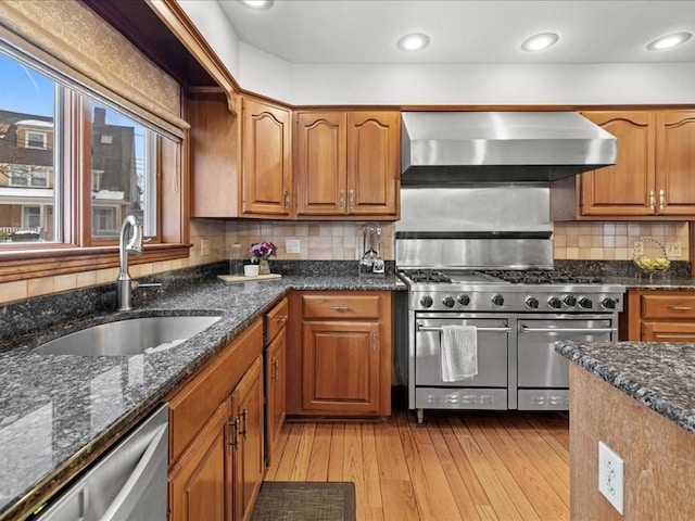 kitchen with wall chimney exhaust hood, brown cabinets, a sink, and stainless steel appliances