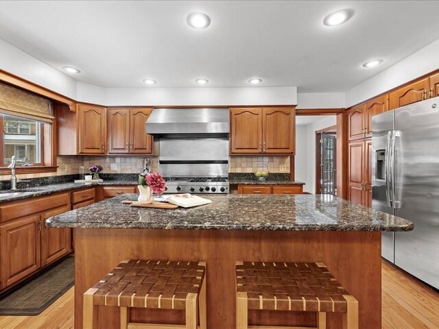 kitchen with a sink, a center island, brown cabinets, wall chimney exhaust hood, and stainless steel fridge