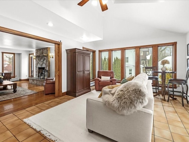 living area featuring a ceiling fan, lofted ceiling, light tile patterned flooring, and a stone fireplace