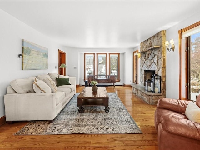 living room with a baseboard radiator, light wood-style flooring, and a stone fireplace