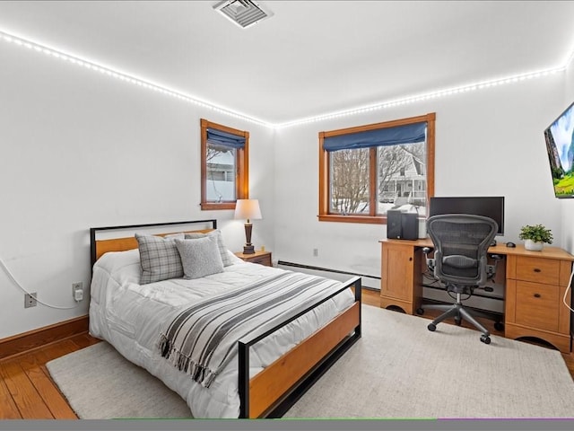 bedroom featuring a baseboard radiator, wood finished floors, visible vents, baseboards, and baseboard heating