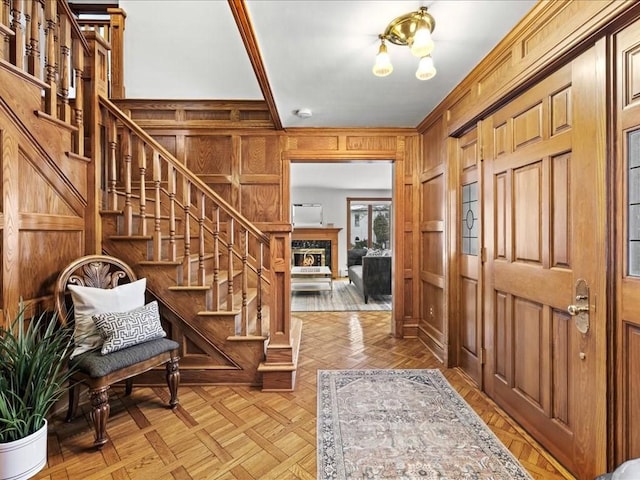 foyer with wood walls, stairs, ornamental molding, and a fireplace