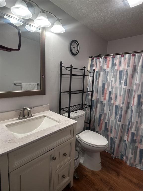 bathroom with hardwood / wood-style floors, vanity, walk in shower, toilet, and a textured ceiling