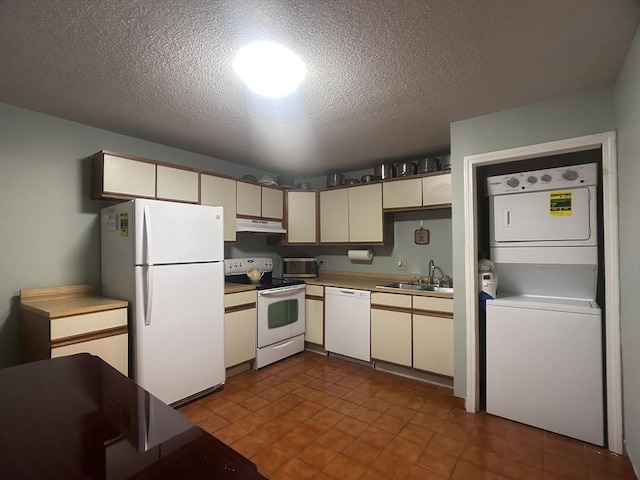 kitchen with sink, white appliances, stacked washer and clothes dryer, cream cabinets, and a textured ceiling