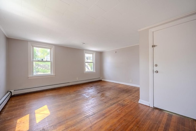 empty room with a baseboard radiator, hardwood / wood-style floors, crown molding, and baseboards