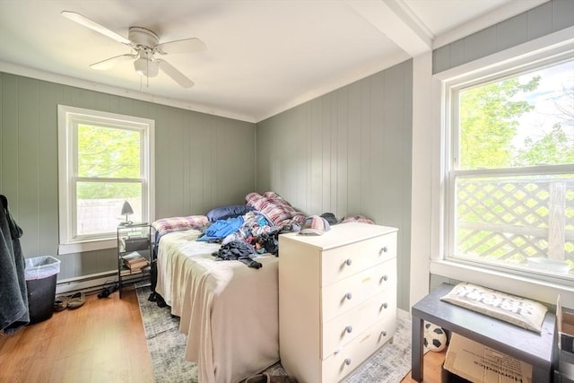 bedroom featuring multiple windows, a baseboard heating unit, light wood-style flooring, and a ceiling fan