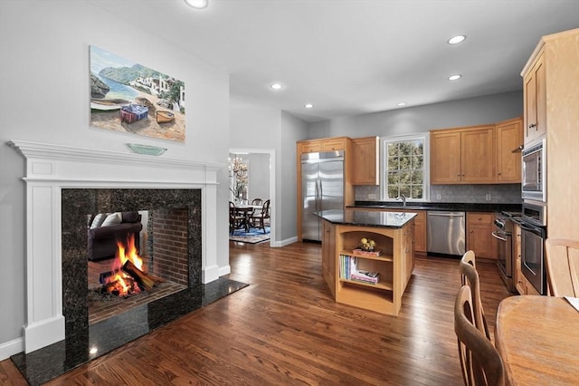 kitchen with a kitchen island, dark wood-style flooring, built in appliances, a sink, and a high end fireplace