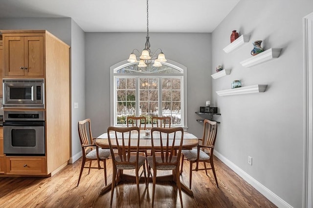 dining space featuring light wood finished floors, baseboards, and an inviting chandelier