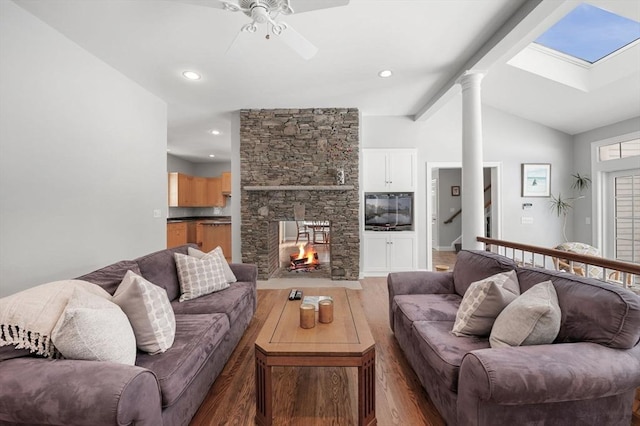 living room featuring vaulted ceiling with skylight, a fireplace, ornate columns, and wood finished floors