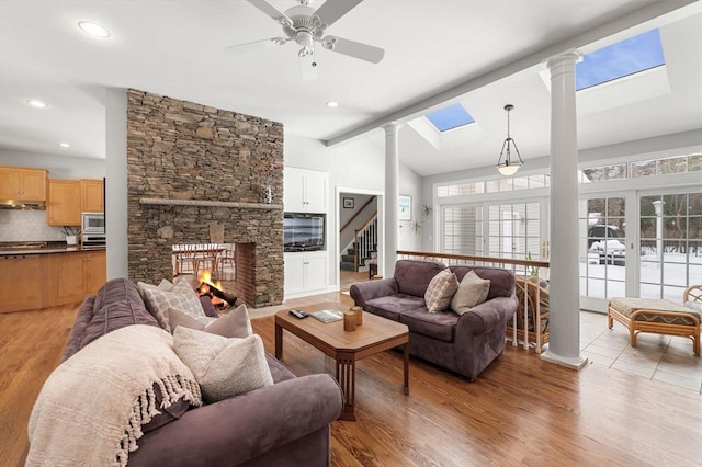 living room with vaulted ceiling with skylight, a stone fireplace, and ornate columns