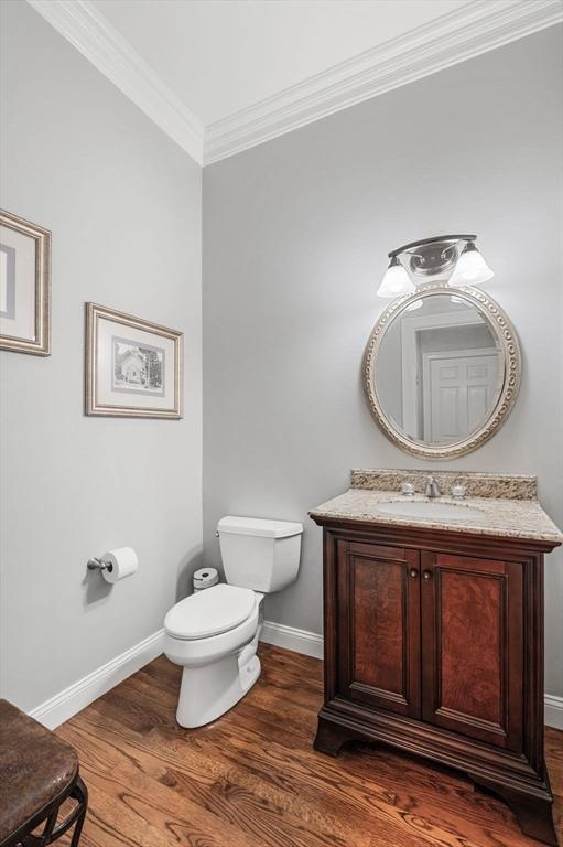 half bathroom featuring baseboards, toilet, ornamental molding, wood finished floors, and vanity