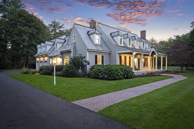 view of front facade featuring a lawn, a chimney, aphalt driveway, an attached garage, and a porch