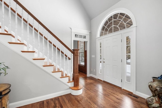 foyer entrance featuring baseboards, visible vents, stairway, wood finished floors, and high vaulted ceiling