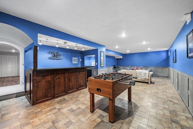 rec room with arched walkways, stone finish flooring, wainscoting, and recessed lighting