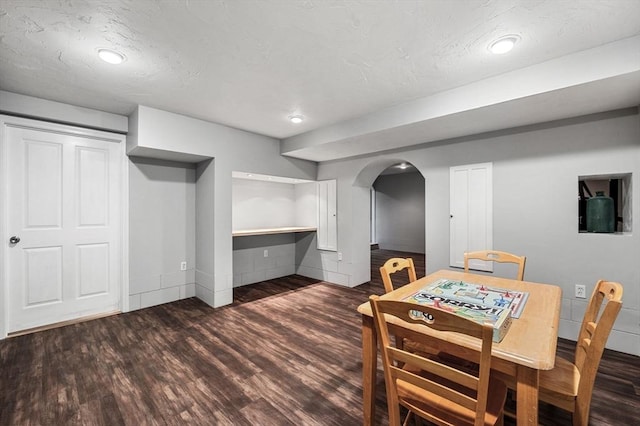 dining room featuring arched walkways, a textured ceiling, and wood finished floors