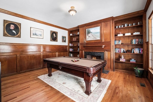 game room featuring ornamental molding, visible vents, a lit fireplace, and light wood finished floors