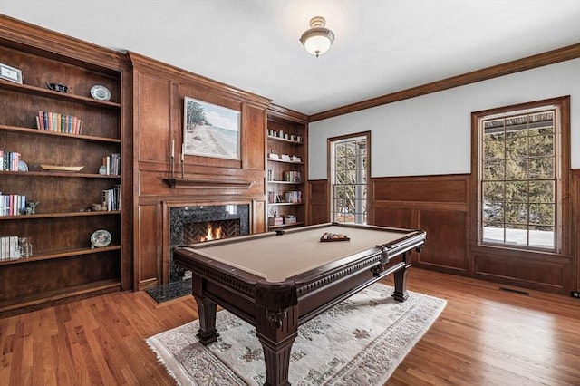 recreation room featuring built in features, a wainscoted wall, visible vents, a high end fireplace, and light wood-type flooring