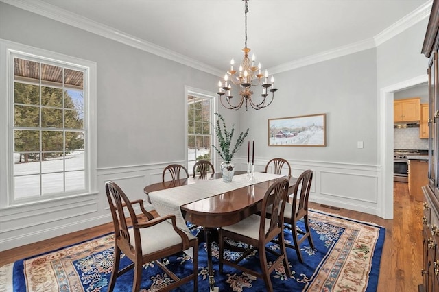 dining area with ornamental molding, a wainscoted wall, an inviting chandelier, and wood finished floors