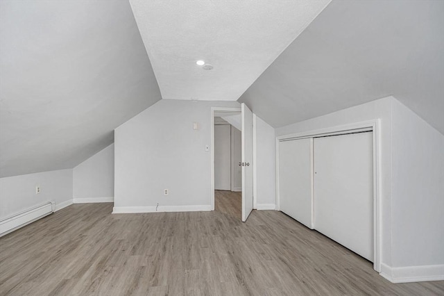 additional living space with lofted ceiling, a textured ceiling, light wood-type flooring, and baseboard heating