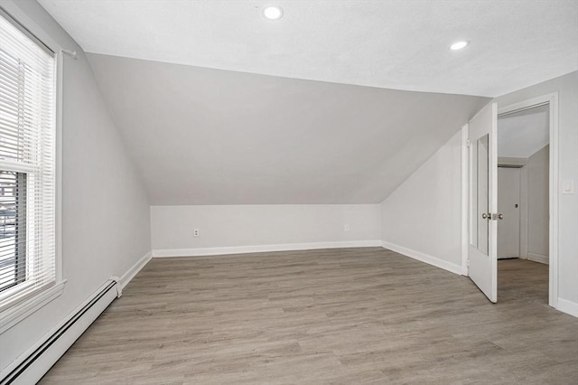 additional living space with light hardwood / wood-style flooring, a wealth of natural light, a baseboard radiator, and vaulted ceiling