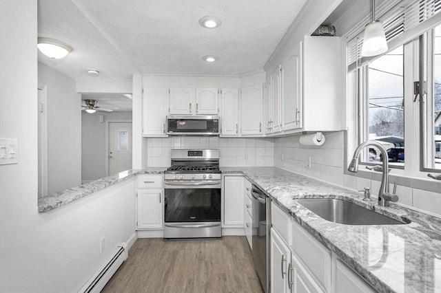 kitchen with sink, light hardwood / wood-style flooring, hanging light fixtures, appliances with stainless steel finishes, and white cabinets