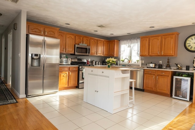 kitchen featuring sink, a kitchen island, light hardwood / wood-style floors, stainless steel appliances, and beverage cooler